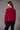 a woman wearing a brushed v-neck red sweater and black jeans on a grey studio background.