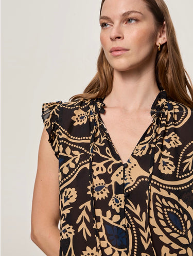 A close-up of a model wearing a sleeveless V-neck blouse with a beige and black paisley pattern, set against a plain light gray background.