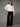 A woman wearing a black ponte pants and a white sweater on a studio background
