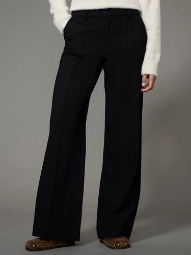 A woman wearing a black ponte pants and a white sweater on a studio background
