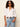Woman wearing a white button-up shirt and blue jeans with sunglasses on a beige background