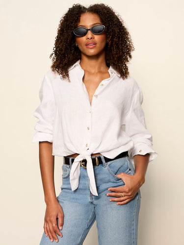 Woman wearing a white button-up shirt and blue jeans with sunglasses on a beige background