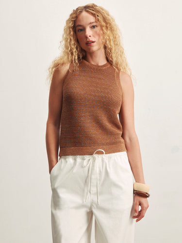Woman wearing a brown sleeveless knitted top and white pants against a light background