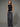 A woman wearing a black boatneck rhinestone tank and black jeans on a grey studio background.