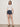 A woman wearing a white top with blue shorts with white stripes and heels on a neutral background