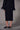 a woman wearing a black sweater with feather cuffs, a mesh midi skirt with a velvet floral pattern and black heels on a grey studio background
