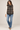 a woman wearing jeans, a white long sleeve top and a plaid vest on a white background.