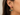 A close-up of a model's ear wearing a gold hoop earring with a semi-circular green stone pendant.
