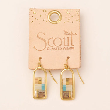 A pair of gold-tone dangle earrings with rectangular wood inlay panels in natural, beige, and light blue tones, displayed on a peach-colored card labeled Scout Curated Wears.