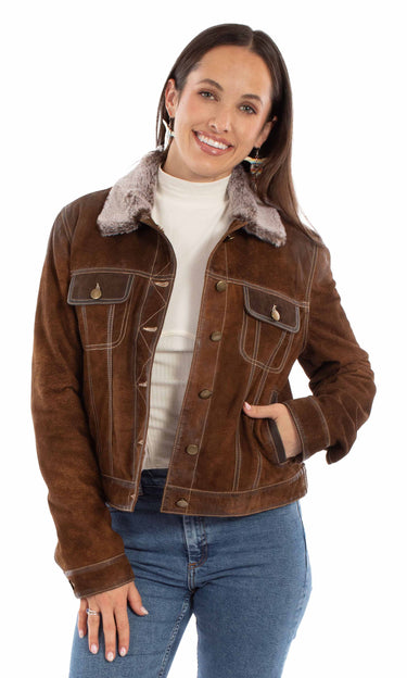 A woman wearing a distressed suede jacket with a faux fur collar and blue jeans on a white background