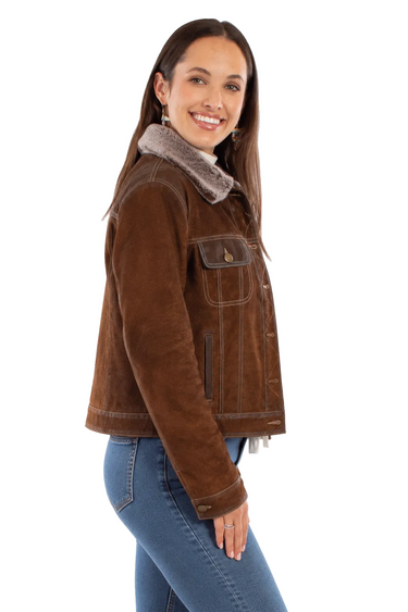 A woman wearing a distressed suede jacket with a faux fur collar and blue jeans on a white background