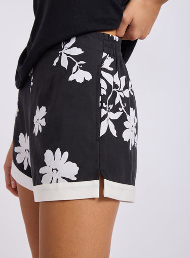 Black shorts with white floral pattern worn by a person on a light gray background