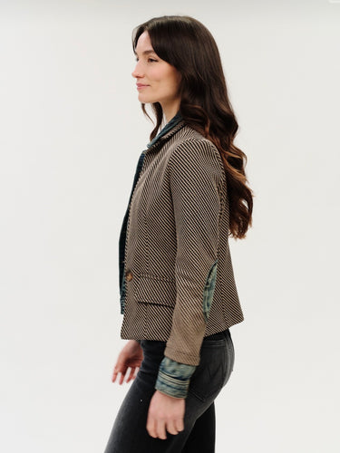 A woman wearing a mixed media jacket that includes checkered denim blazer with a denim jacket sleeves and elbow patches on a white background.