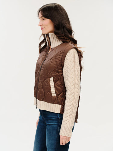 a woman wearing a mixed media jacket that consists of a brown vest and knit sleeves and collar on the jacket.