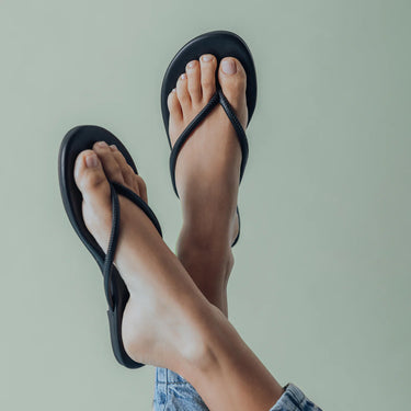 Black sandals worn on feet against a light green background