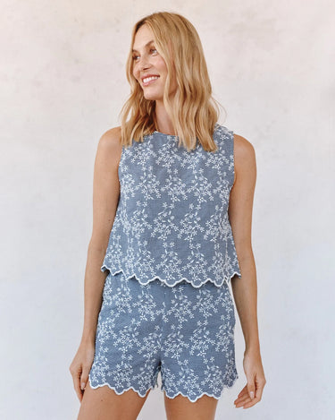 Woman wearing a blue floral sleeveless top and shorts set against a plain background