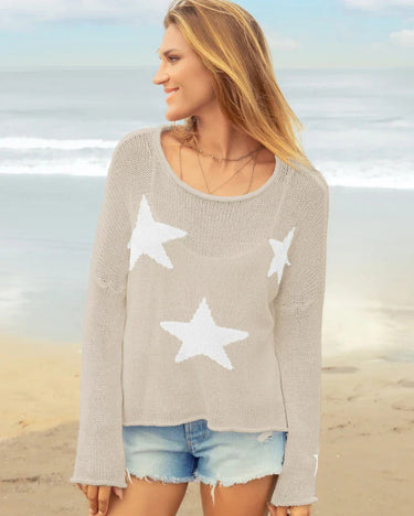 Woman wearing a light brown sweater with white star patterns on a beach.