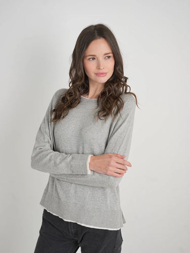 a woman wearing a light grey charcoal sweater with black jeans on a white background