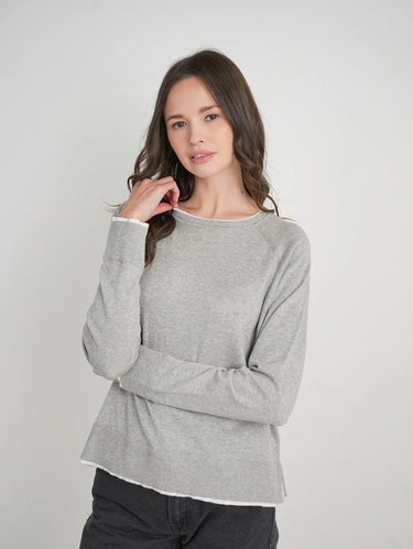 a woman wearing a light grey charcoal sweater with black jeans on a white background