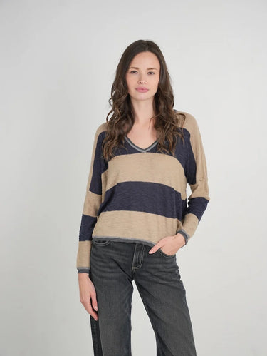 a woman wearing a beige and navy stripe sweater and black jeans on a neutral background