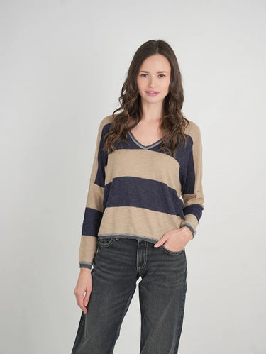 a woman wearing a beige and navy stripe sweater and black jeans on a neutral background