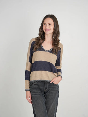 a woman wearing a beige and navy stripe sweater and black jeans on a neutral background