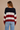 Person wearing a black, red, and white striped sweater with blue jeans on a beige background