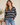 A woman wearing a navy and beige striped long-sleeve henley sweater with blue jeans, standing in a brightly lit indoor setting.