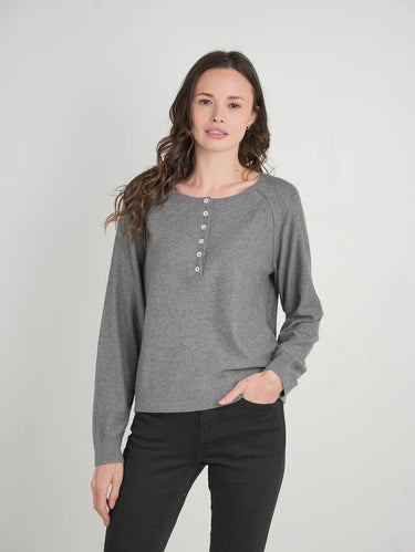 A woman modeling a heather gray long-sleeve henley top with a buttoned neckline, paired with black pants, against a light gray studio background.