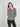 A woman modeling a gray long-sleeve knit top with a buttoned neckline, paired with black pants, against a plain light gray studio background.