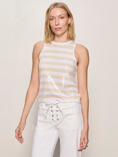 A woman wearing a striped beige and white sequin top with white pants on a neutral background