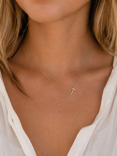 a woman wearing a horizontal gold cross necklace