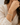 A close-up of a woman wearing a delicate silver bangle bracelet with small gold and white inlay details, paired with a cream-colored textured blouse.