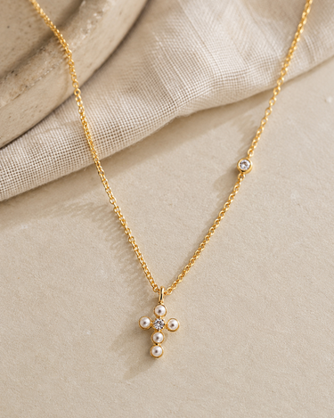 a close up of the pearl cross necklace on a flat surface
