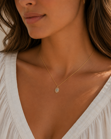 a woman wearing an oval pearl and opal pendant on a gold chain