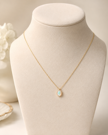 A delicate gold chain necklace with a teardrop-shaped white opal pendant, displayed on a cream-colored jewelry bust.