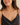 A close-up of a woman wearing a delicate gold chain necklace with a small, round, iridescent white pendant, styled with a black camisole top against a soft beige background.