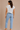 A woman wearing a cotton cream v neck blouse with blue stripes and jeans on a neutral background