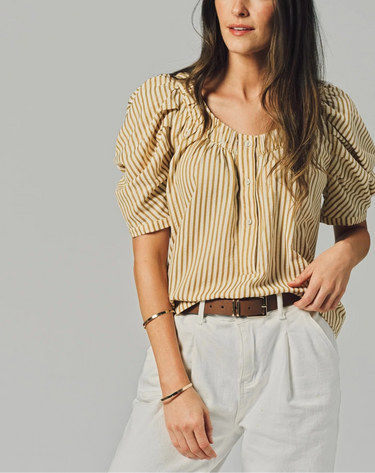 Woman wearing a striped blouse and white pants against a gray background
