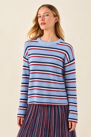 A woman wearing a light blue ribbed knit sweater with horizontal navy and red stripes, paired with a matching striped skirt, against a solid beige background.