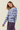 A woman modeling a light blue knit sweater with horizontal navy and red stripes, paired with a matching striped skirt, against a solid light beige background.