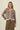 A woman modeling a fuzzy leopard-print cardigan with brown buttons, paired with olive green pants, against a plain cream background.