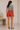 Woman wearing a striped shirt and orange shorts standing in a minimalistic room.