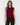 A woman modeling a sleeveless cropped vest in deep burgundy with dark buttons and flap chest pockets, paired with black pants, against a light gray studio background.