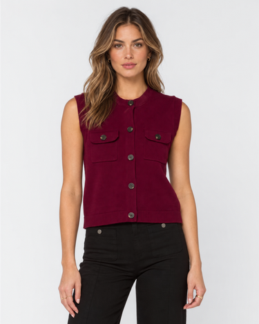 A woman modeling a sleeveless cropped vest in deep burgundy with dark buttons and flap chest pockets, paired with black pants, against a light gray studio background.