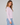 A woman wearing a long sleeve crew neck tee in lavender with blue jeans on a neutral background.