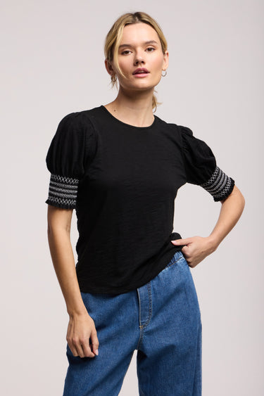 a woman wearing a black blouse with smocked puff sleeves and jeans on a neutral background