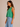 A woman wearing a boxy cotton cropped tank in shamrock green and blue jeans on a neutral background