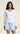 A woman modeling a white long-sleeve V-neck top and light blue shorts against a plain beige studio background.