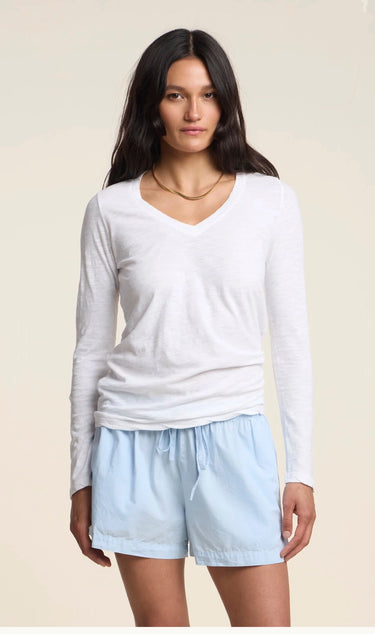 A woman modeling a white long-sleeve V-neck top and light blue shorts against a plain beige studio background.